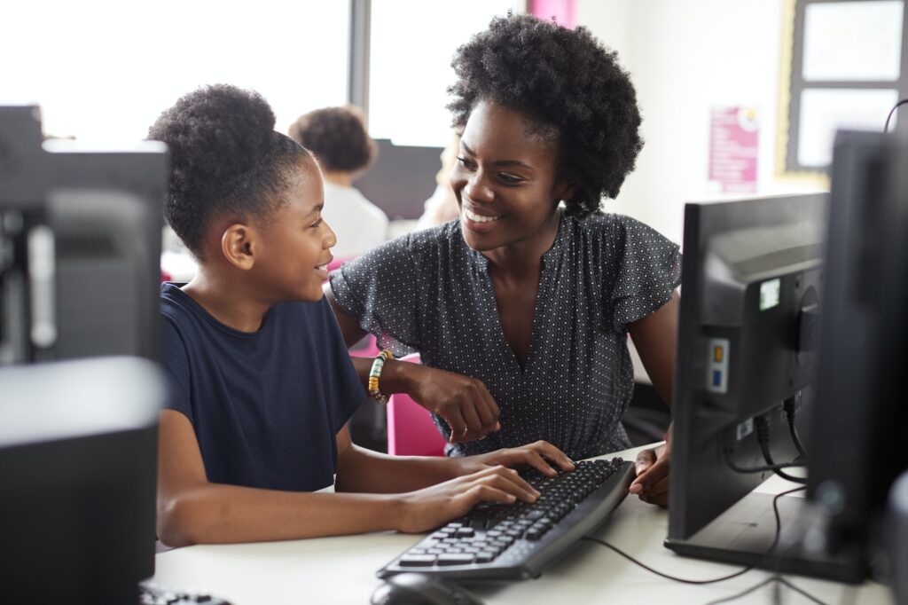 Teacher Helping Female High School Student Working at Screen In Computer Class